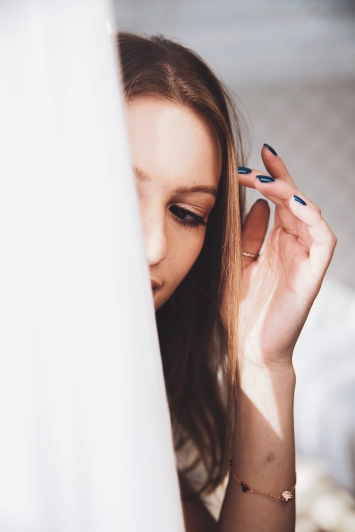woman holding her hair in front of white curtain